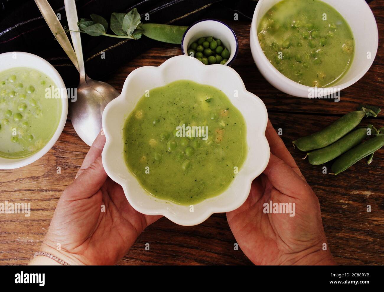 Fresh green pea soup with pea seeds and pea pods around , top view