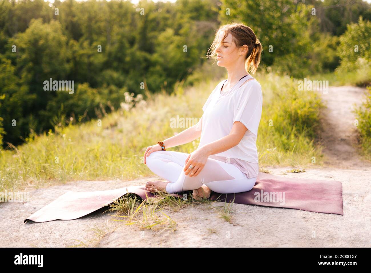 Young woman meditating sitting on yoga mat in lotus position with ...