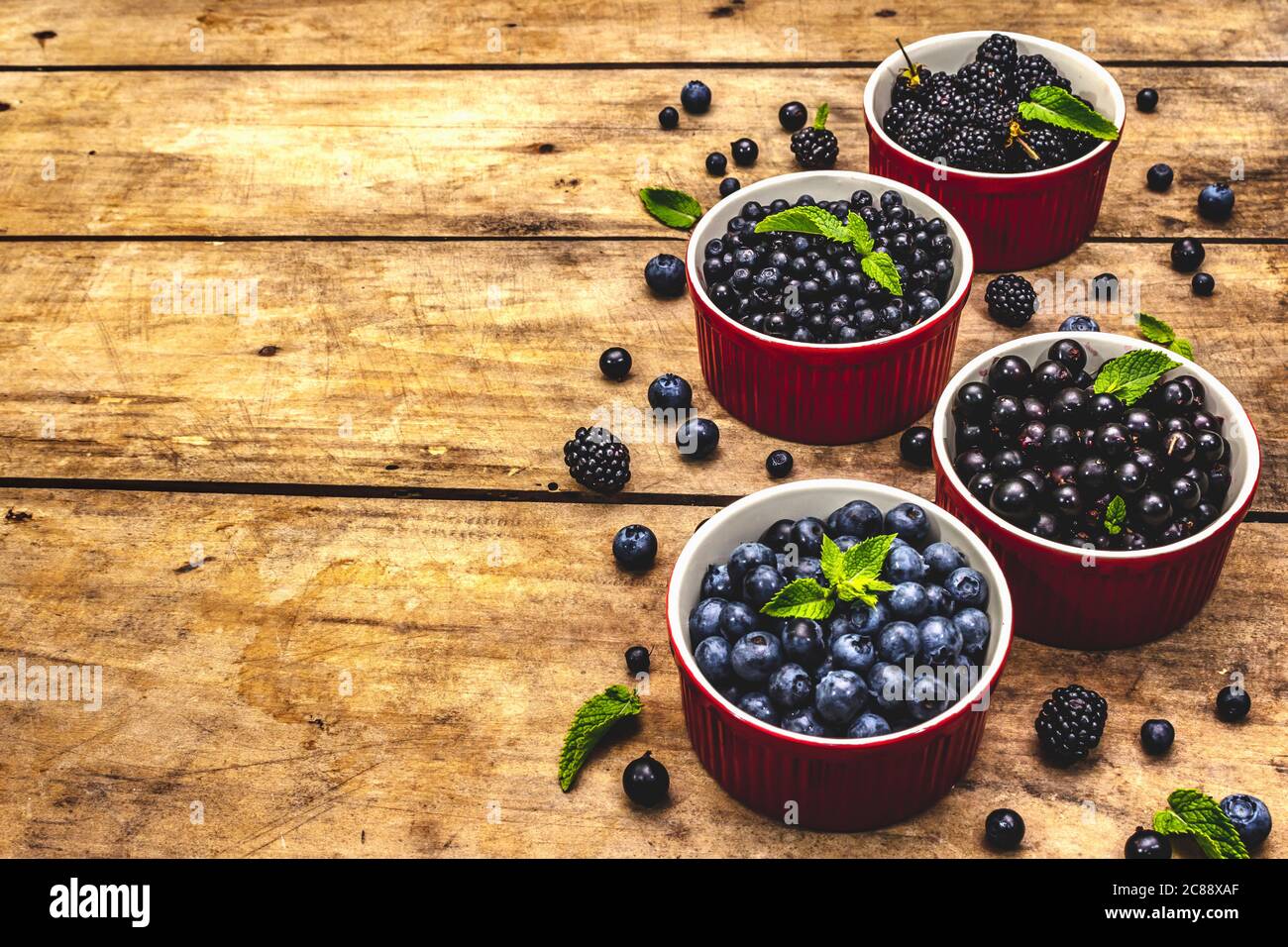 Assorted berries in blue and black colors: bilberry, blueberry, currant and blackberry. Old wooden table background, copy space Stock Photo