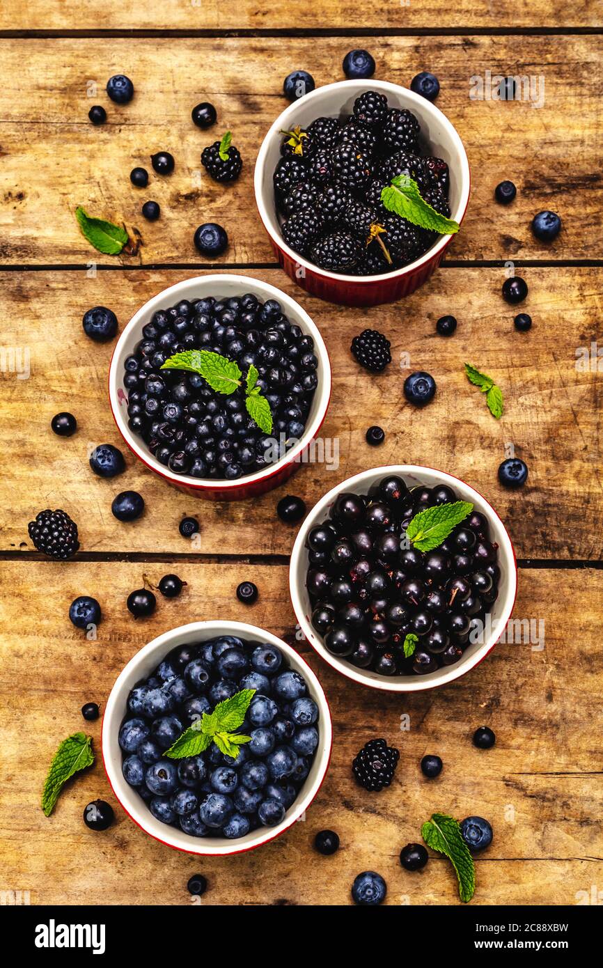 Assorted berries in blue and black colors: bilberry, blueberry, currant and blackberry. Old wooden table background, top view Stock Photo