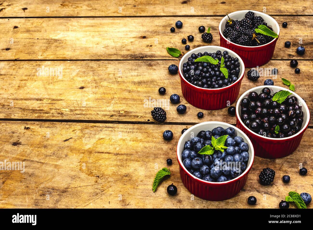 Assorted berries in blue and black colors: bilberry, blueberry, currant and blackberry. Old wooden table background, copy space Stock Photo