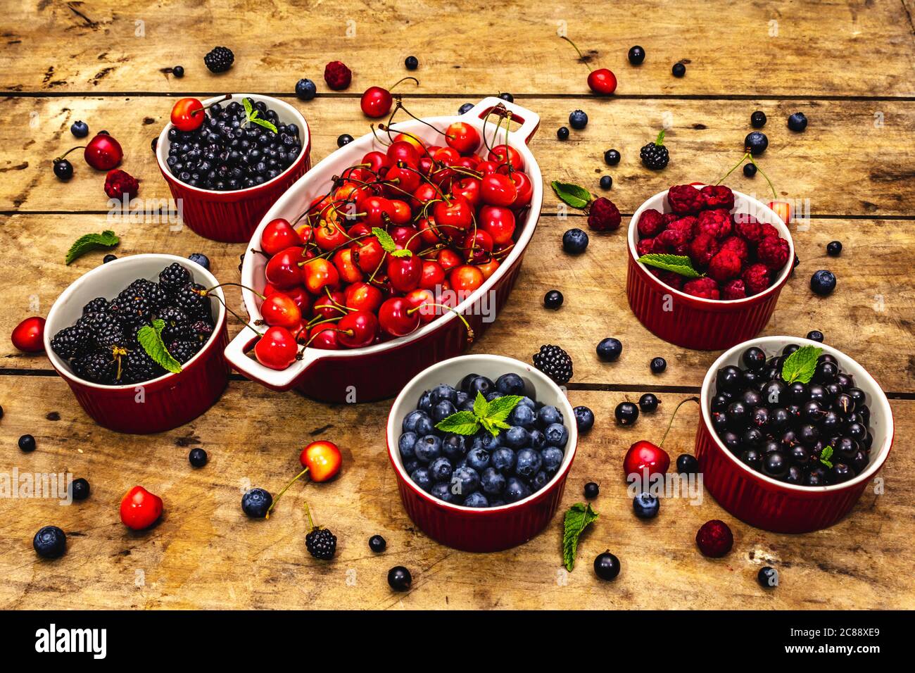Assorted berries in bowls: bilberry, blueberry, currant, blackberry, cherry and raspberry. Old wooden table background, close up Stock Photo