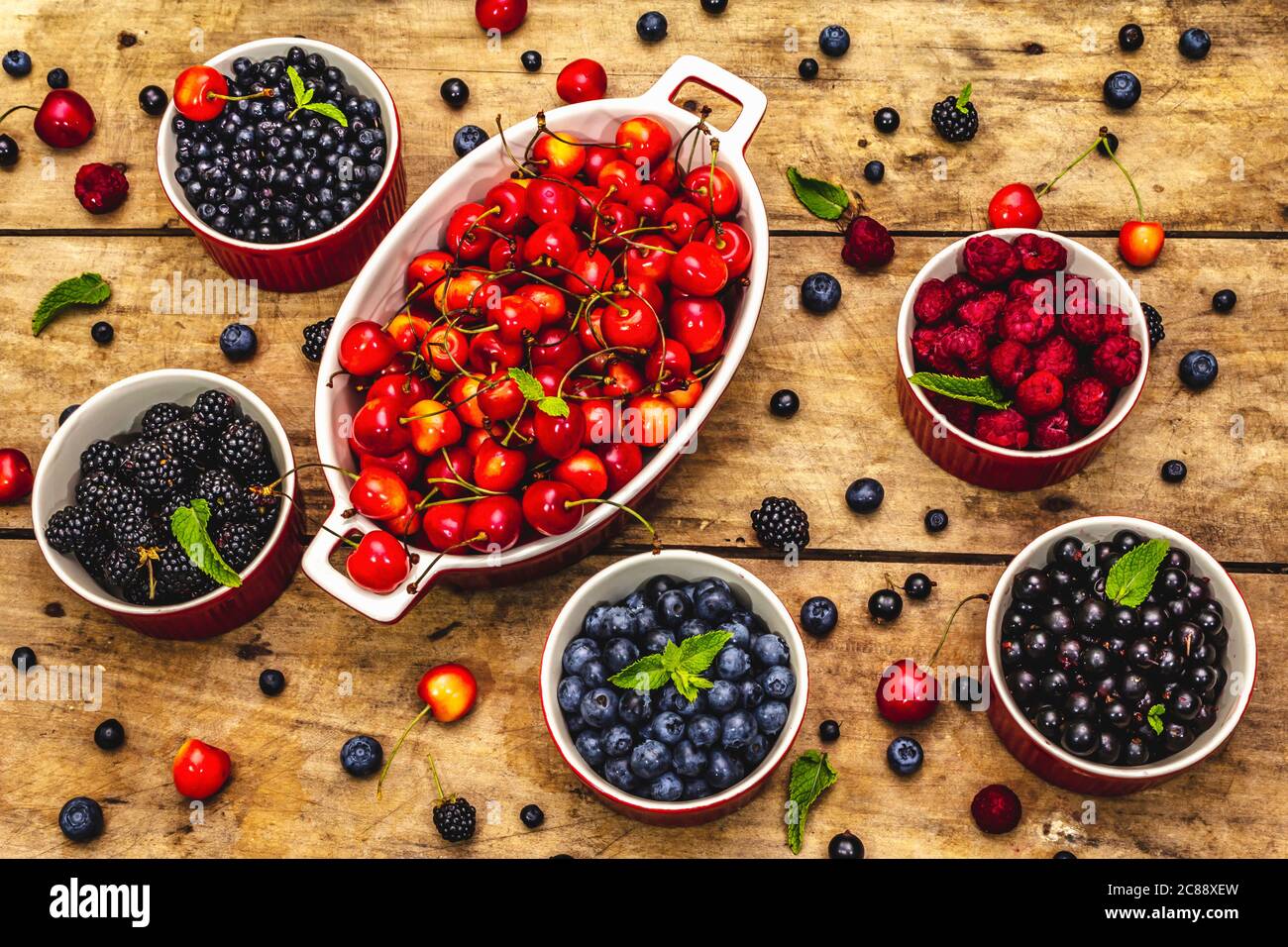 Assorted berries in bowls: bilberry, blueberry, currant, blackberry, cherry and raspberry. Old wooden table background, top view Stock Photo