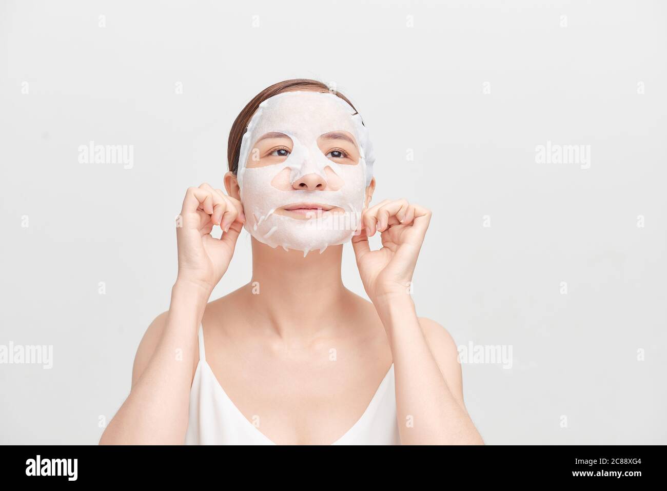 Young girl with facial mask looking at camera over white background. Cosmetic procedure. Beauty spa and cosmetology. Stock Photo