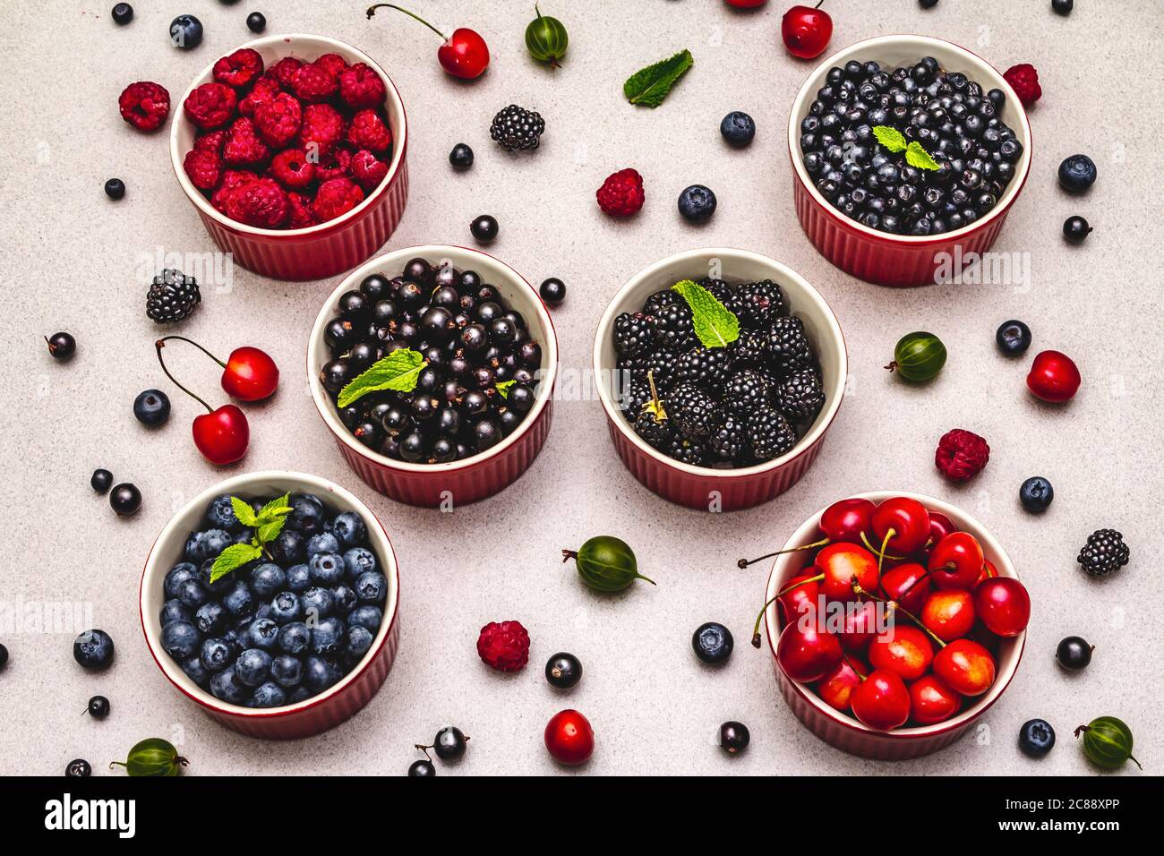 Assorted berries in bowls: bilberry, blueberry, currant, blackberry, cherry and raspberry. Stone concrete background, top view Stock Photo