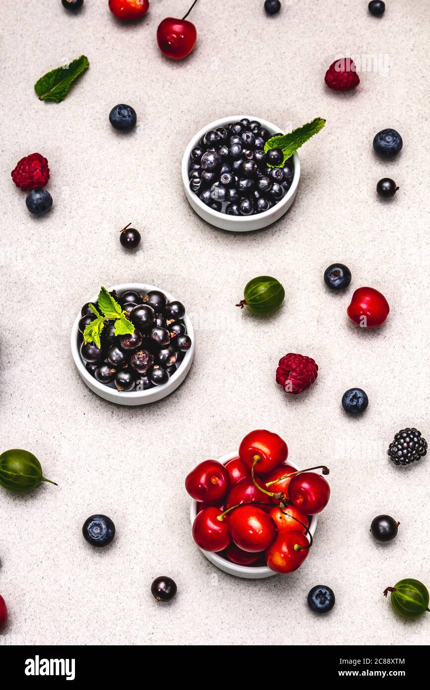 Assorted berries in bowls: bilberry, blueberry, currant, blackberry, cherry and raspberry. Stone concrete background, top view Stock Photo