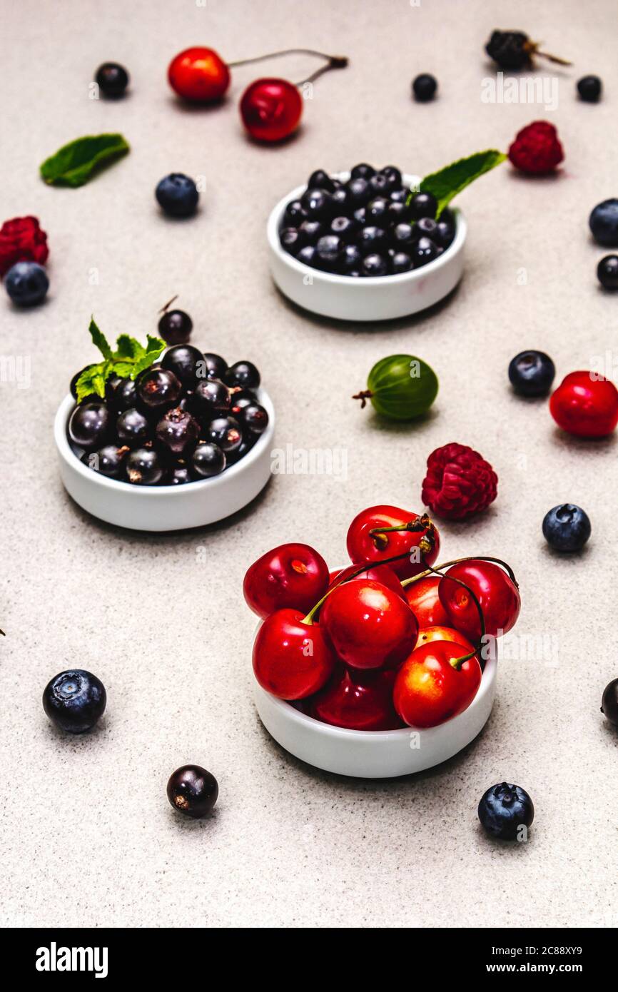 Assorted berries in bowls: bilberry, blueberry, currant, blackberry, cherry and raspberry. Stone concrete background, close up Stock Photo