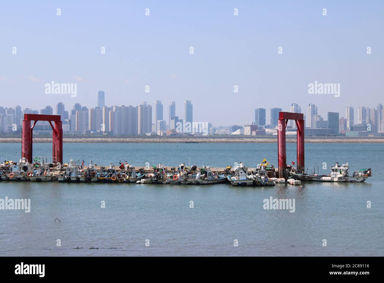 Panorama of colorful fishing boats in an industrial marina, with an urban skyline in the distance, in Oido, Korea Stock Photo