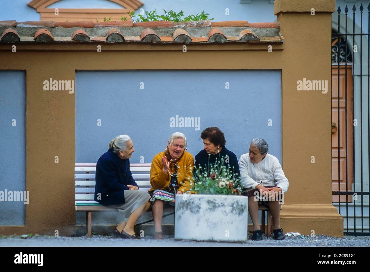 Four elderly Italian ladies sitting on a public bench having a discussion. Italy Stock Photo