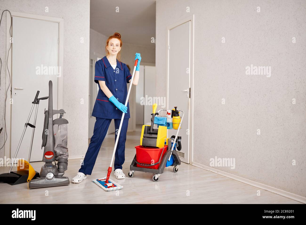 Pleased cheerful redhead maid woman holding mop pile, cleaning floor at