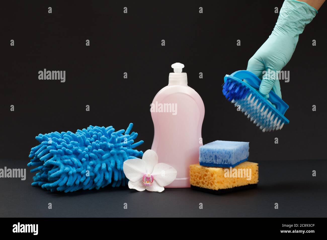 Plastic bottle of dishwashing liquid, a rag, sponges and a hand in a