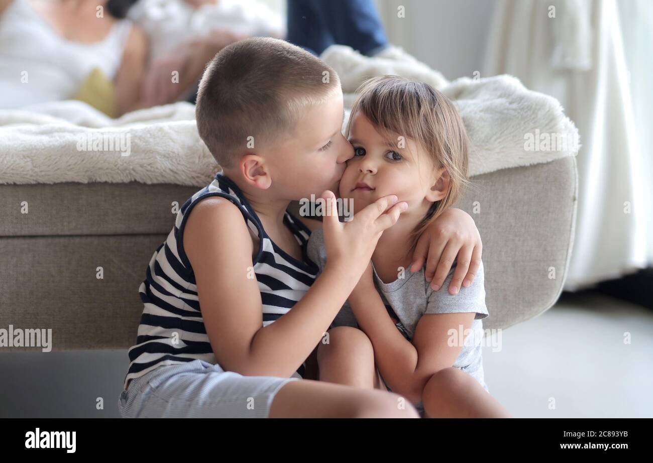 Young kid kissing his sister's cheek under the lights with a blurry background Stock Photo