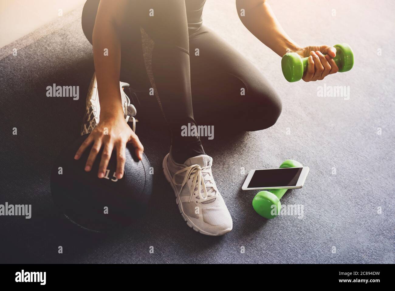 Sporty woman using smartphone during workout at home in the living room.Online personal trainer or on mobile phone.Sport and recreation concept. Stock Photo