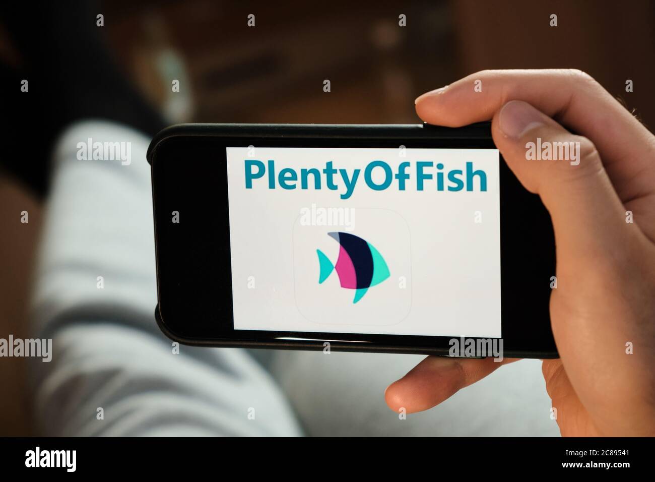 Plenty of fish application on the smartphone in mans hand. Man laying ...