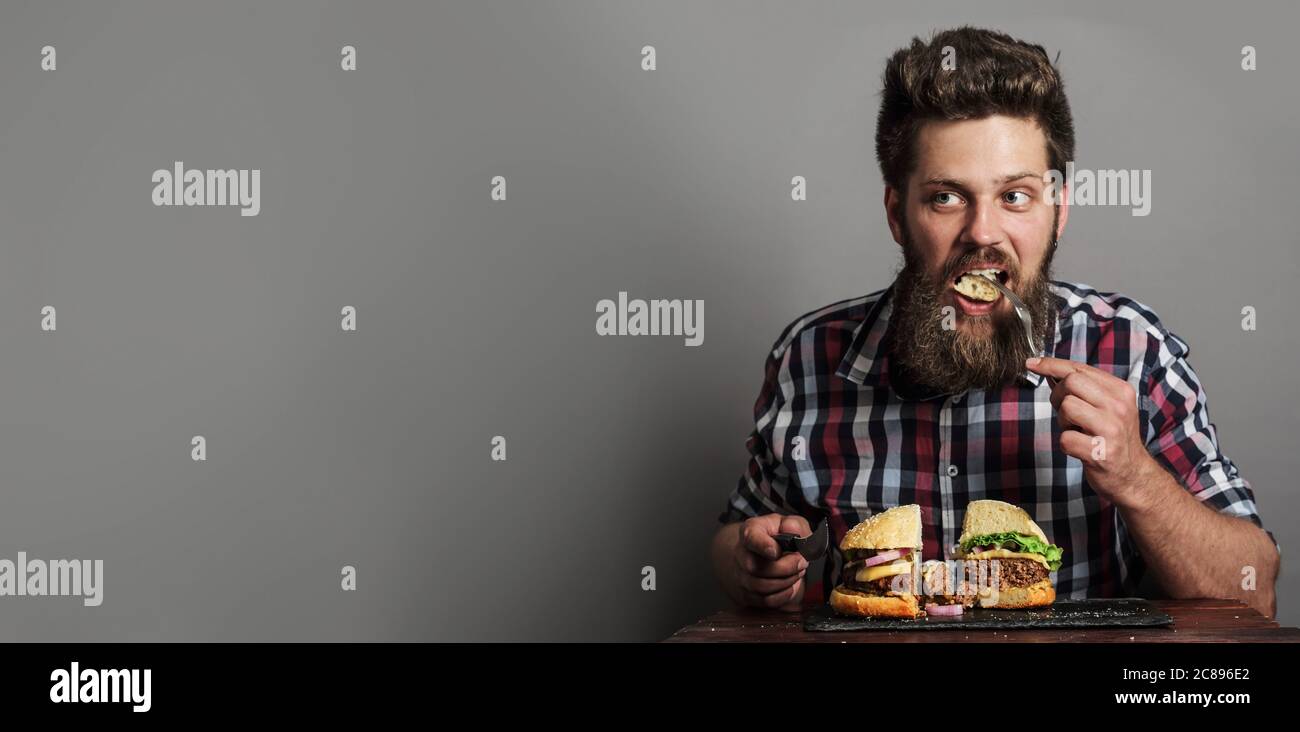 Young man eating fresh tasty large hamburger, gray background with copy space Stock Photo