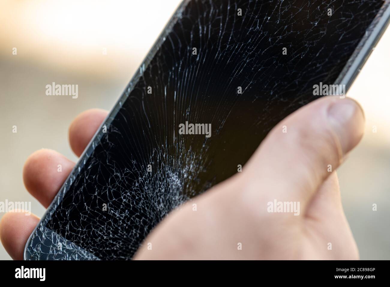 A young man is holding a phone with a very cracked touch screen Stock Photo