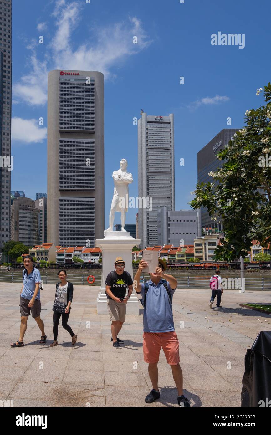 Taking selfies in front of statue of Sir Thomas Raffles by the Singapore River with skyscrapers and shophouses in the background Stock Photo