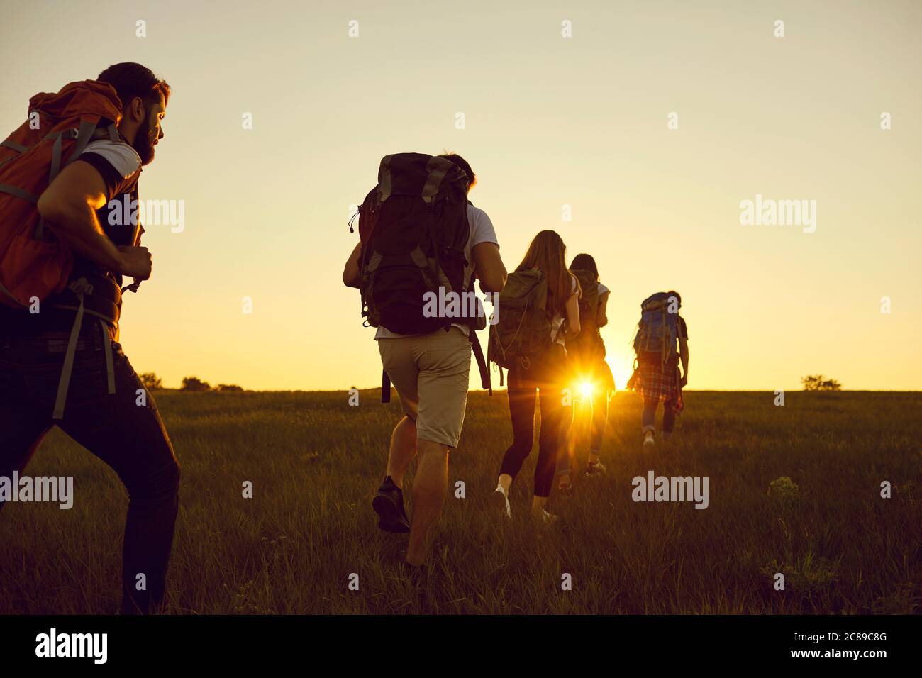 Hike. Hiking. Tourism.A group of tourists with backpacks are walking along the hill at sunset in nature in summer. Stock Photo