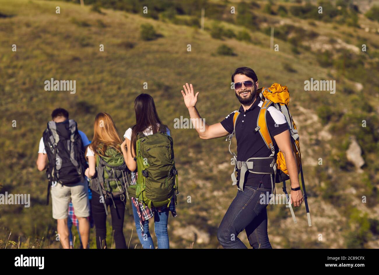A group of hikers with backpacks are walking along the hill in the mountains in nature. Stock Photo