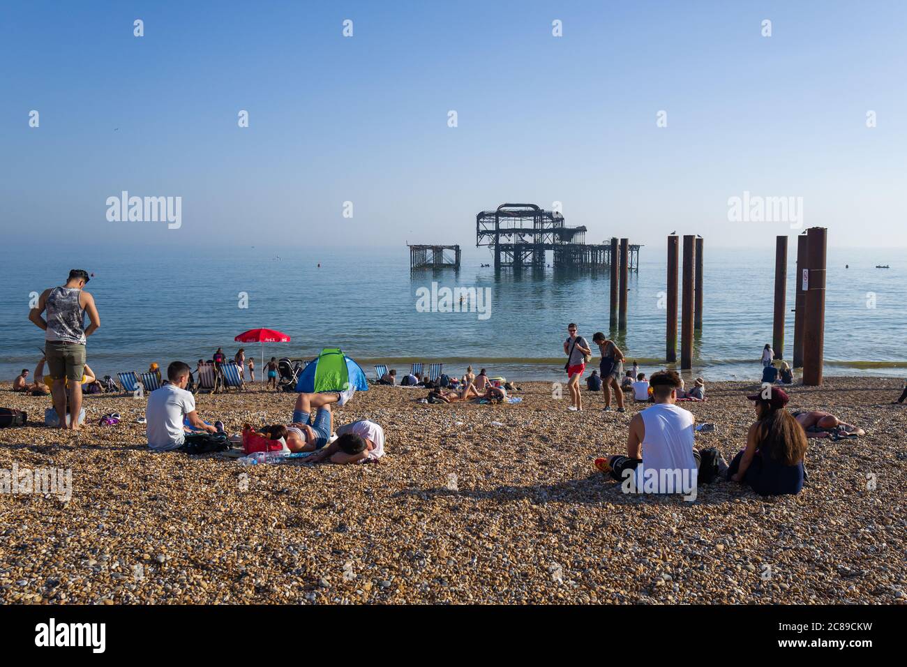 People sunbathing on Brighton's shingle beach by the remains of the West Pier Stock Photo