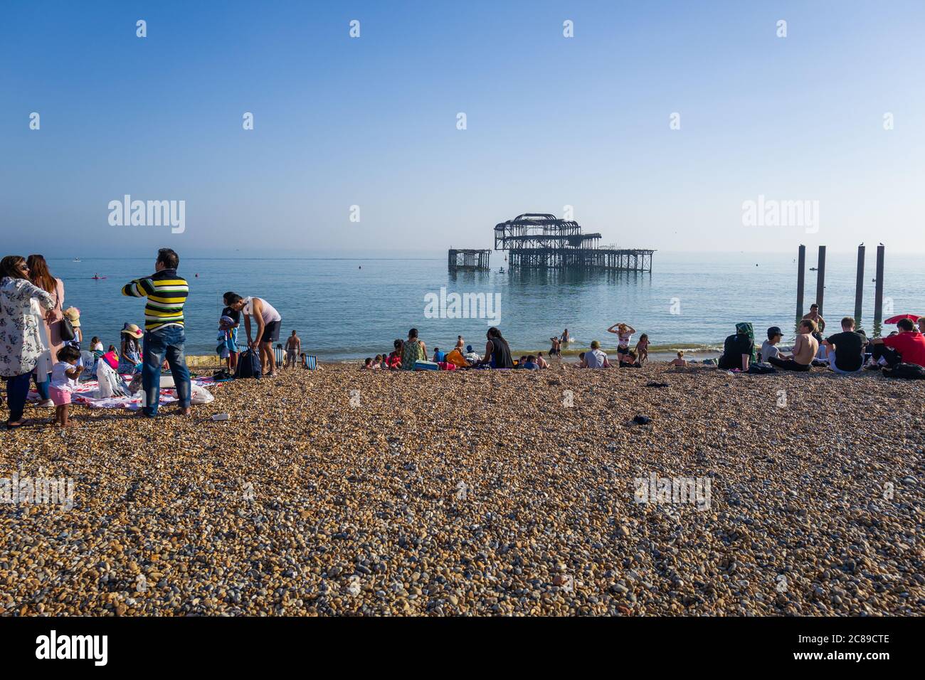 People sunbathing on Brighton's shingle beach by the remains of the West Pier Stock Photo