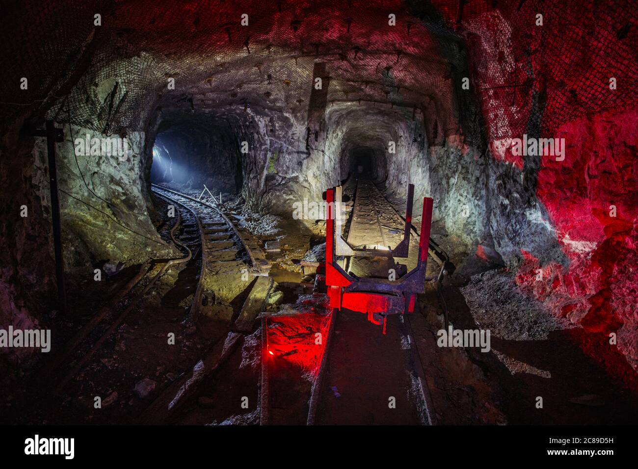 Dark abandoned uranium mine with rusty rail and trolley, red illuminated Stock Photo