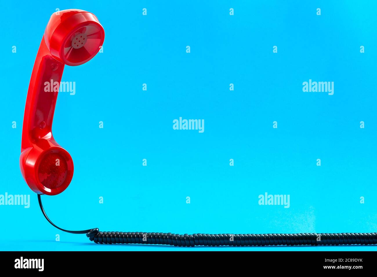 Contact us concept and floating phone receiver with a vintage red telephone handset floating above the curly cable isolated on blue background with co Stock Photo
