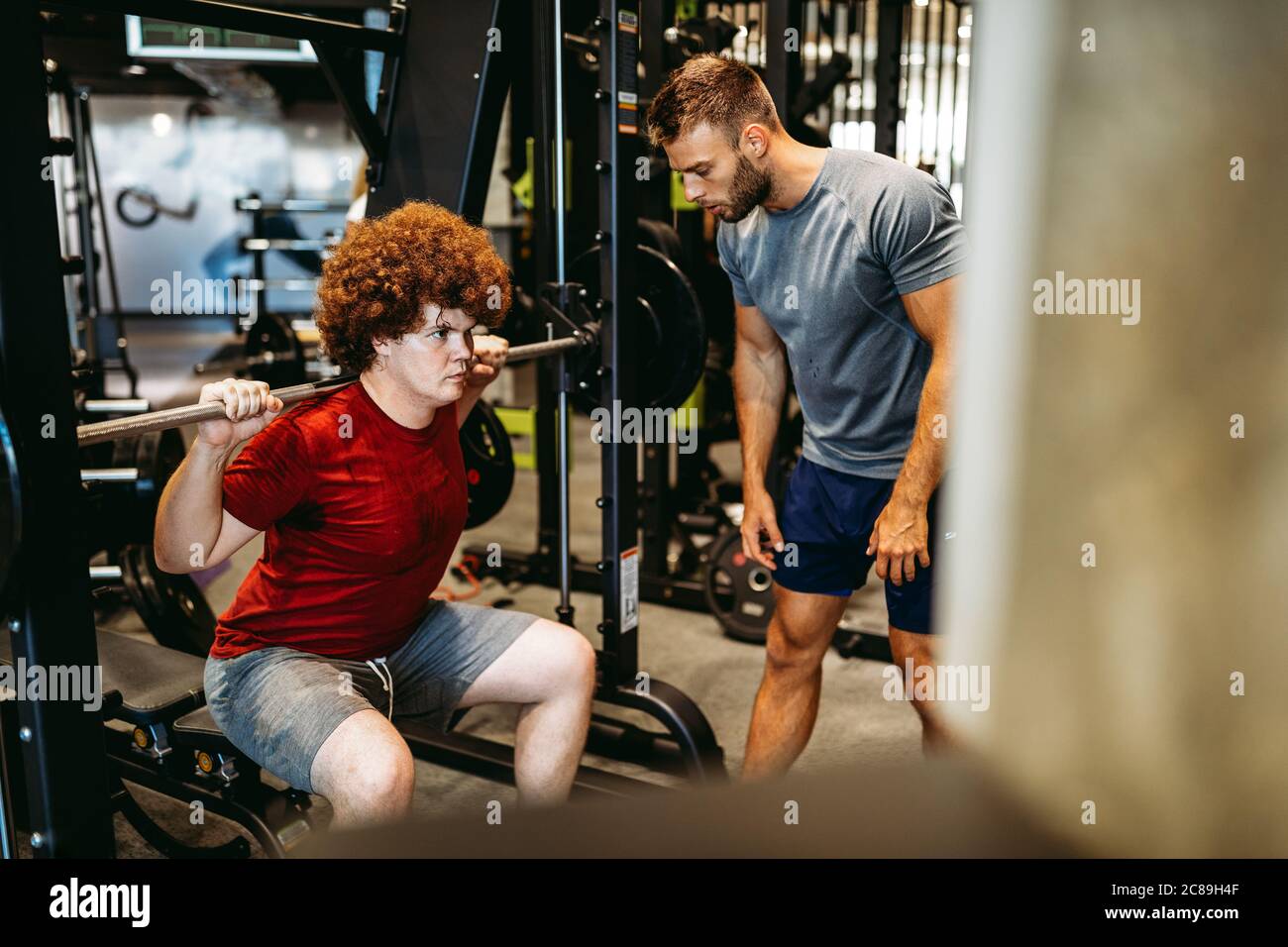 Overweight young man with trainer exercising in gym Stock Photo