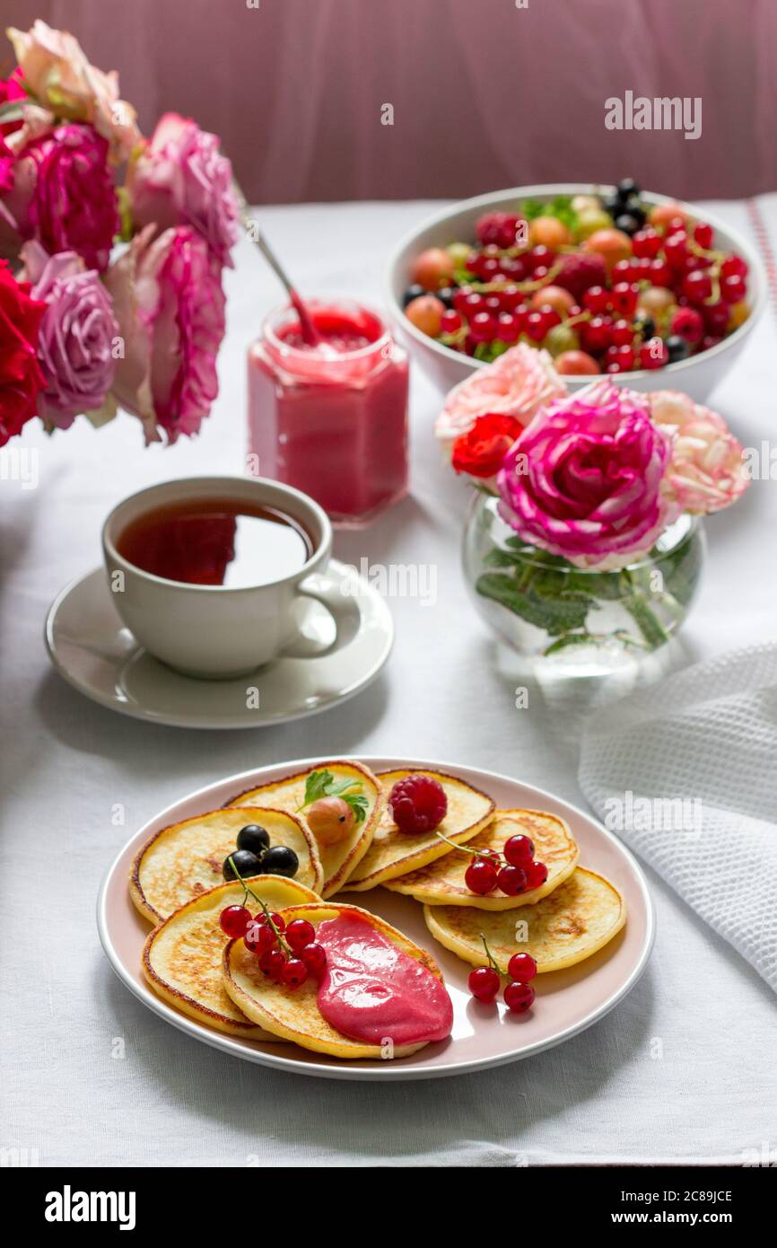 Curd pancakes with berry curd served with tea on a table decorated with bouquets of roses. Stock Photo