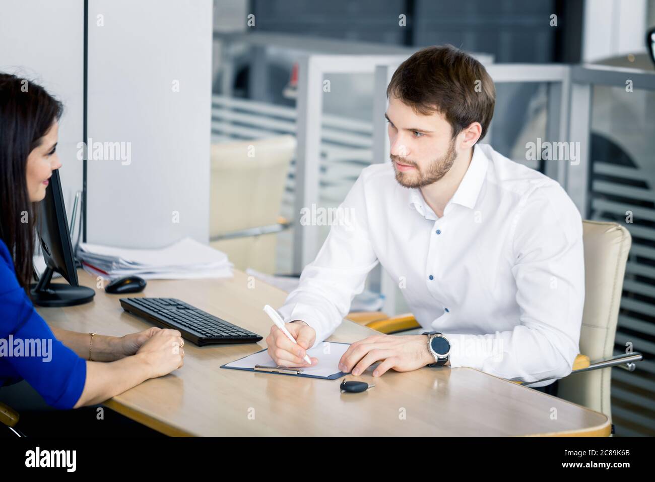 Dealer discussing with potential buyer features of new car in auto salon Stock Photo