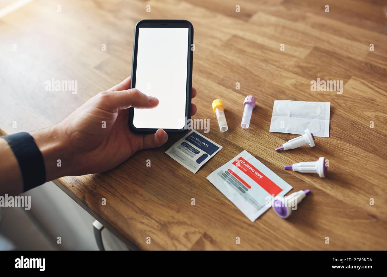 Home blood test kit with blank phone screen on wooden table in mans hands. Stock Photo