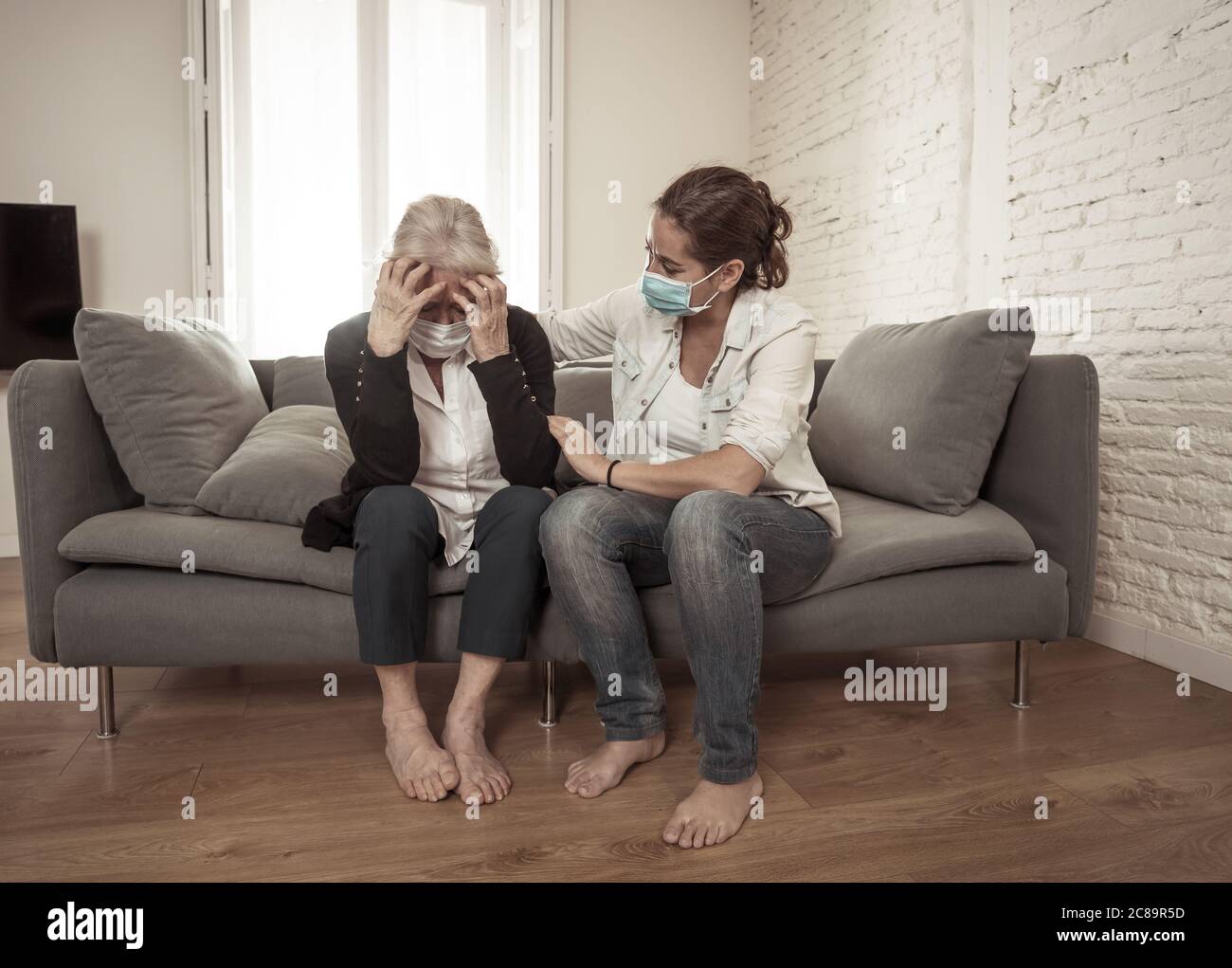 Depressed senior mother and daughter wearing medical mask crying and embracing each other grieving loss of loved ones fighting the Coronavirus. People Stock Photo