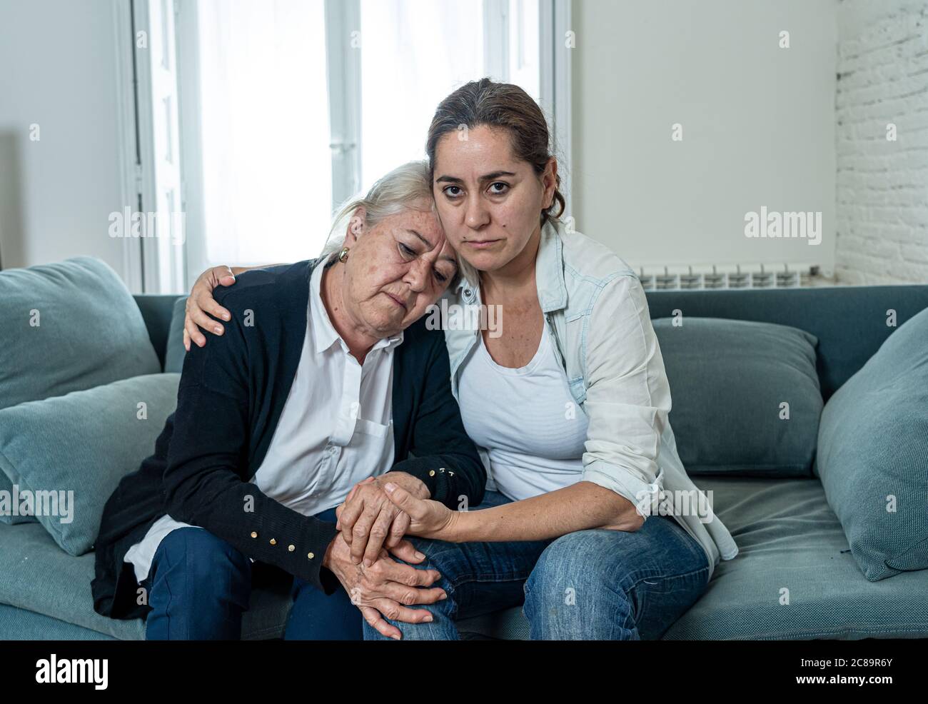 Depressed senior mother and daughter embracing each other grieving loss of loved ones amid Coronavirus pandemic. Two sad women at home in lockdown in Stock Photo