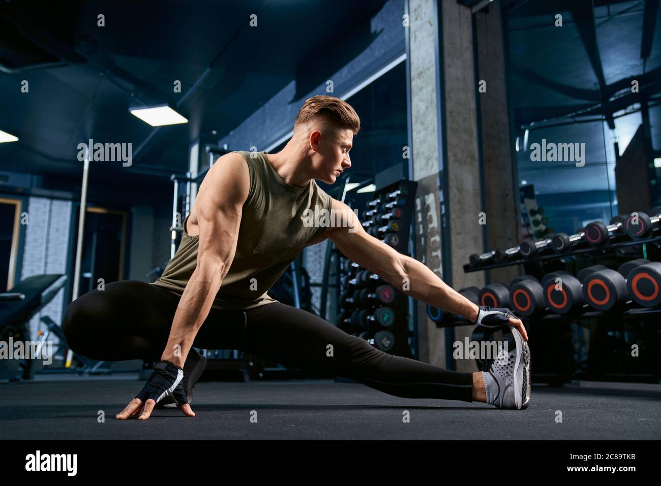 Muscular caucasian bodybuilder in sportswear stretching on floor in sports  club. Front view of handsome young sportsman posing in empty gym. Concept  of bodybuilding, healthy lifestyle Stock Photo - Alamy
