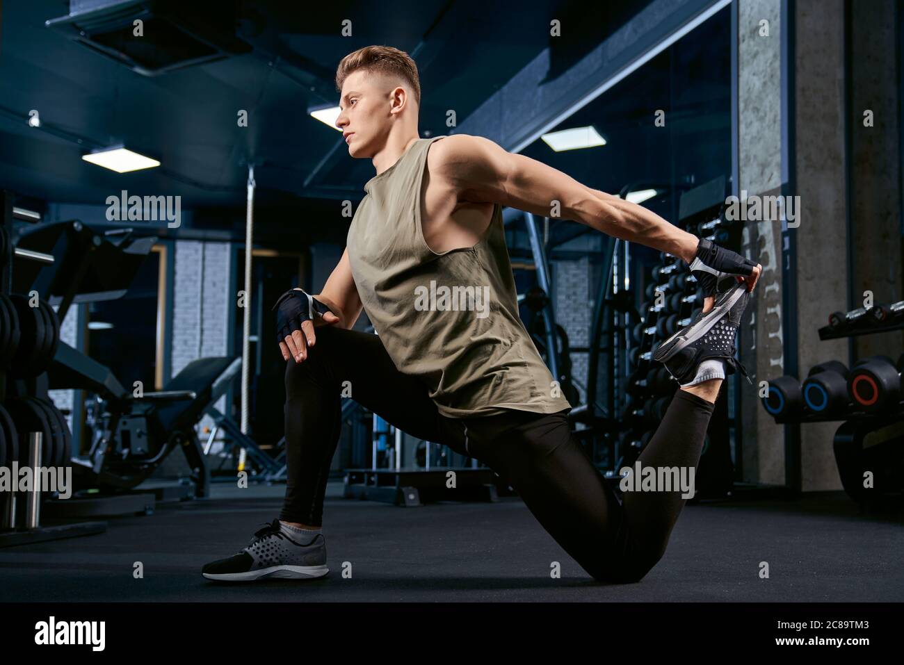 Handsome caucasian bodybuilder in sportswear stretching on floor in sports  club. Side view of muscular sportsman posing in empty gym. Concept of  bodybuilding, healthy lifestyle Stock Photo - Alamy