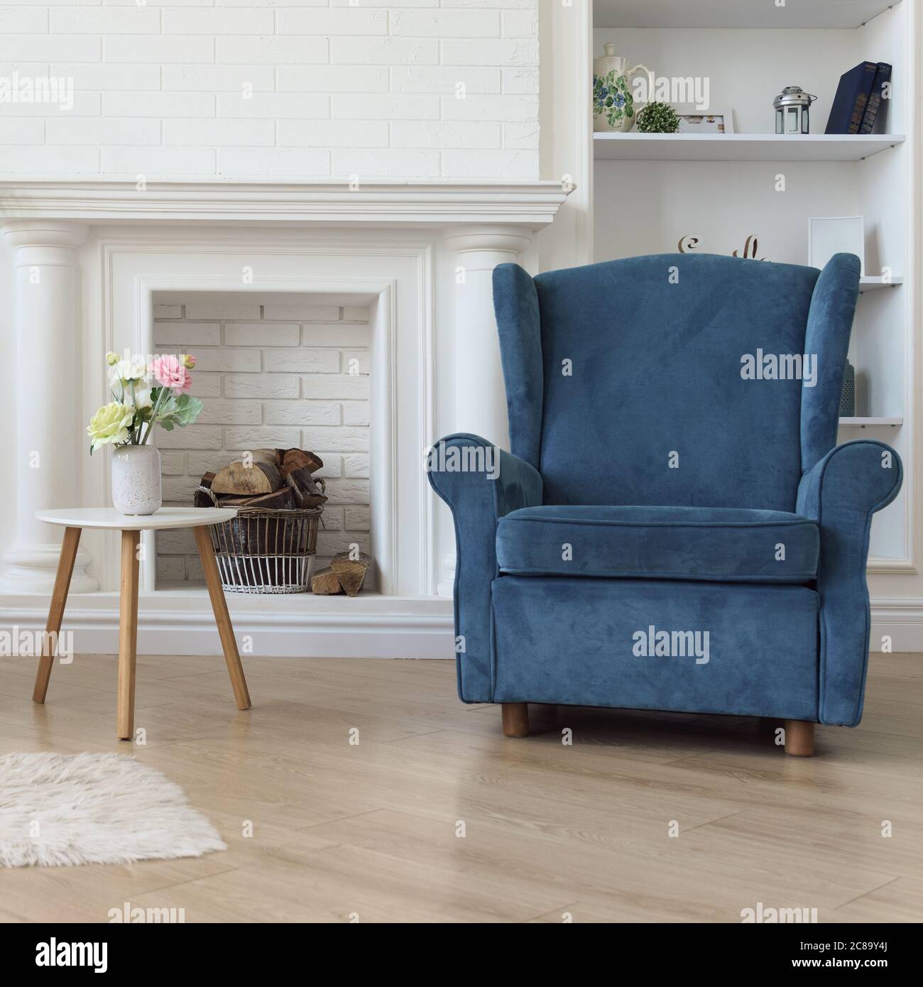 Navy blue classic armchair and flower vase on modern white wooden table in front of fireplace Stock Photo