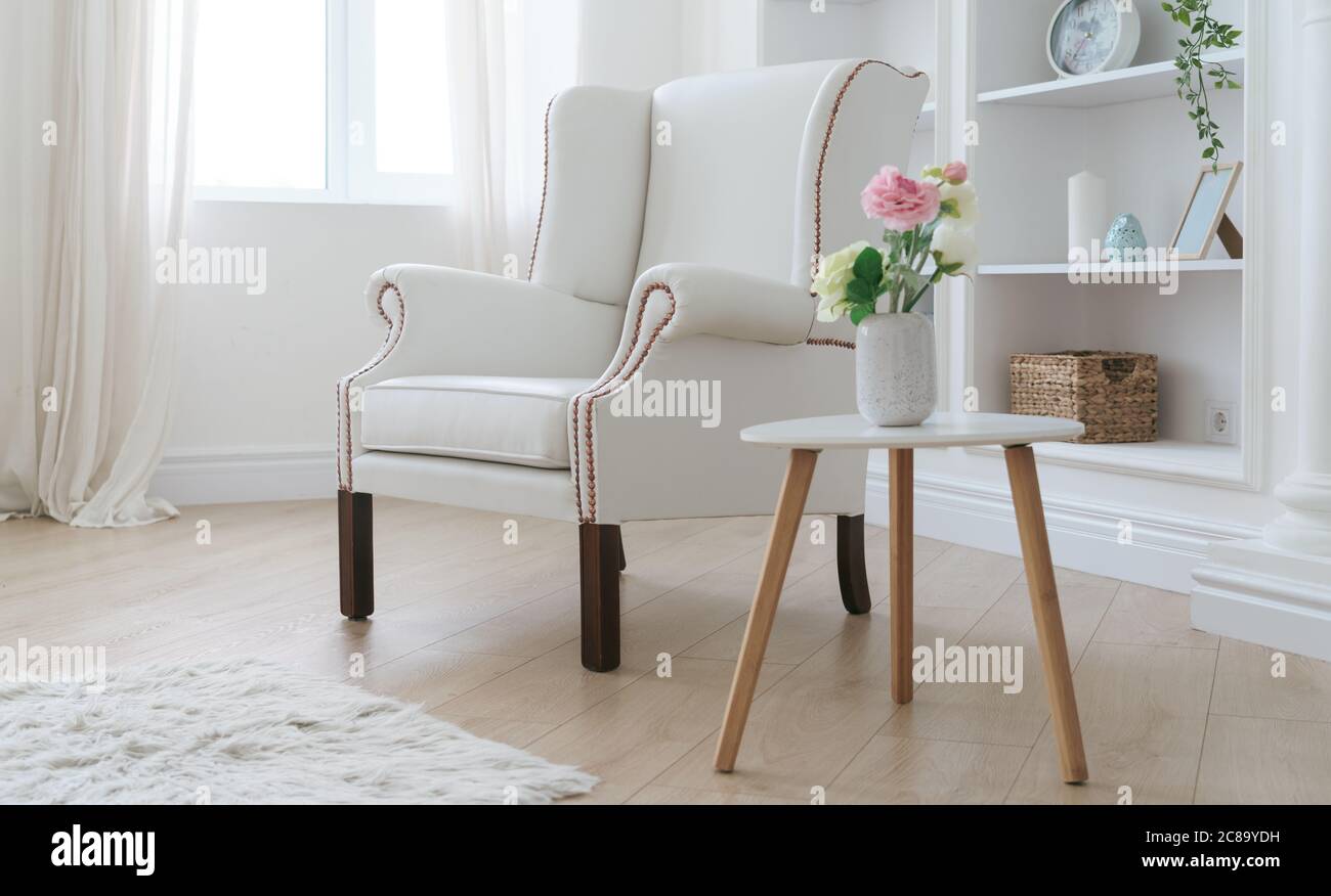 Leather white armchair and modern wooden table with flowers vase in bright room Stock Photo