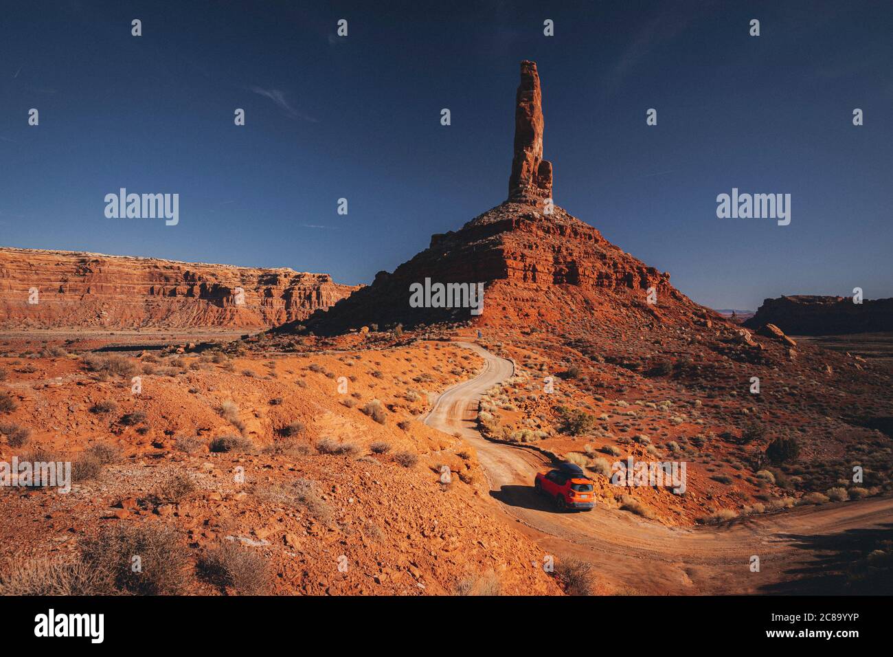An orange car is driving through the Valley of Gods, Utah Stock Photo