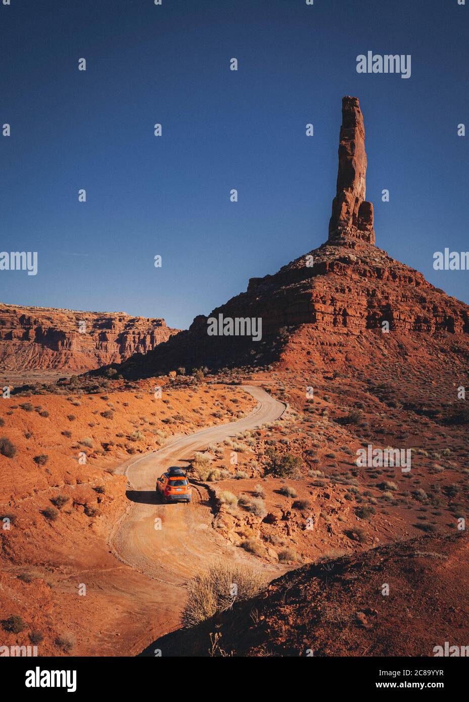 An orange car is driving through the Valley of Gods, Utah Stock Photo