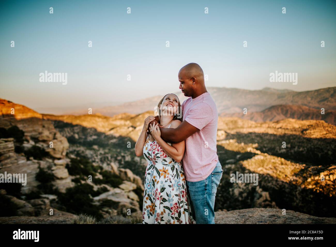 Biracial Couple hugging and looking at each other on a mountain top Stock Photo