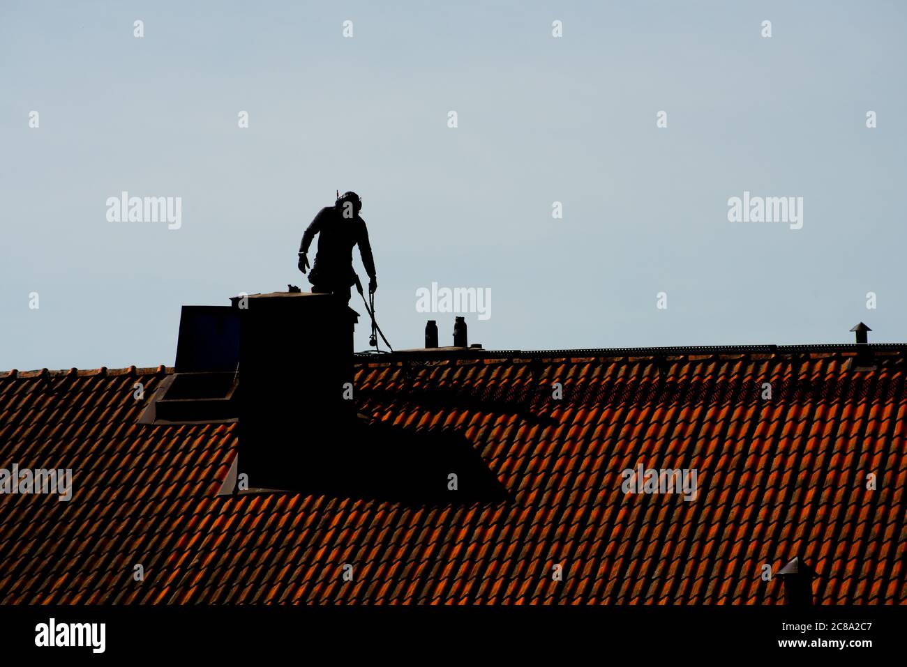 Silhouette of a chimney sweeper on top of a roof. Stock Photo