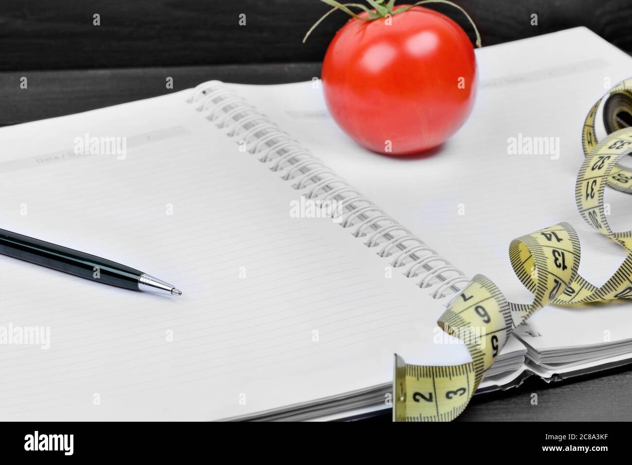 Close up of empty notebook with pen, centimeter and cherry tomato on a wood background Stock Photo