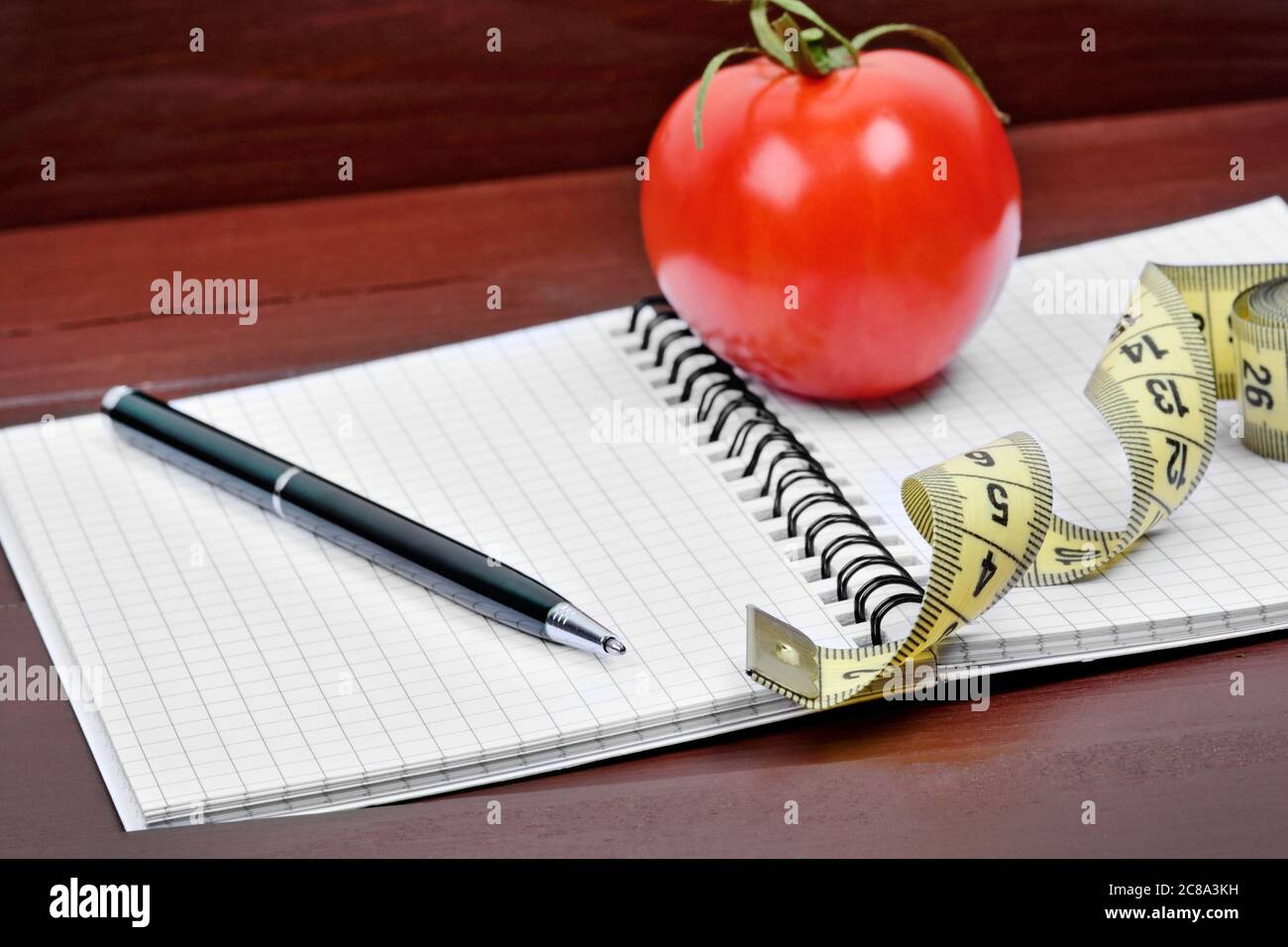 Notebook with pen, centimeter and cherry tomato on a wood background. Diet concept Stock Photo