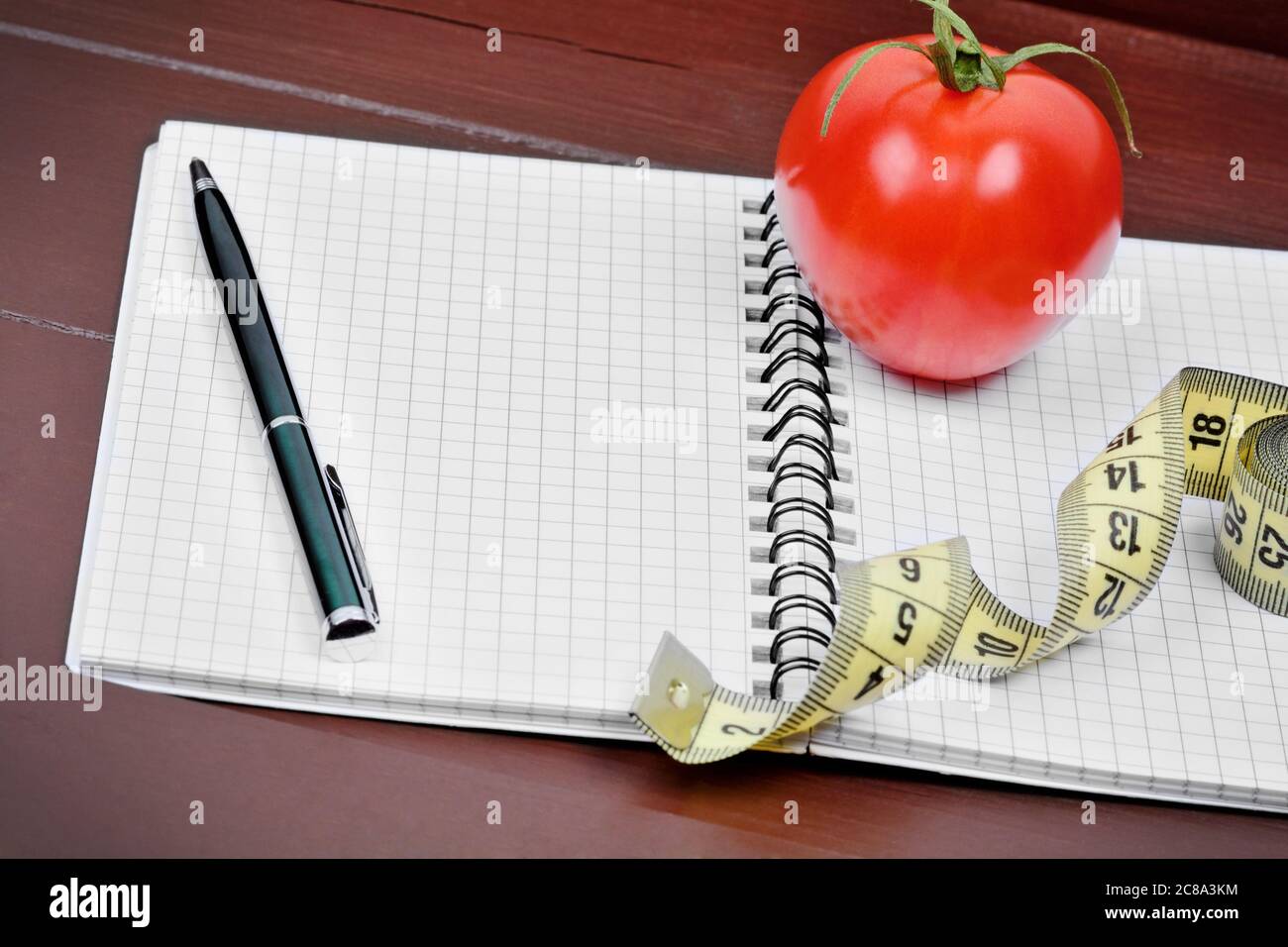 Close up of notebook with pen, centimeter and cherry tomato on table Stock Photo