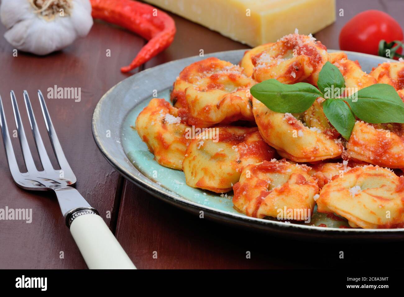 Tortellini with tomatoes sauce and parmesan in a plate on wooden table Stock Photo