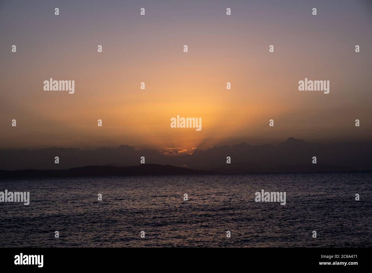 Seascape in Aegean sea, Greece after sunset. Dark island land and orange sky cloudscape over sea water. Stock Photo
