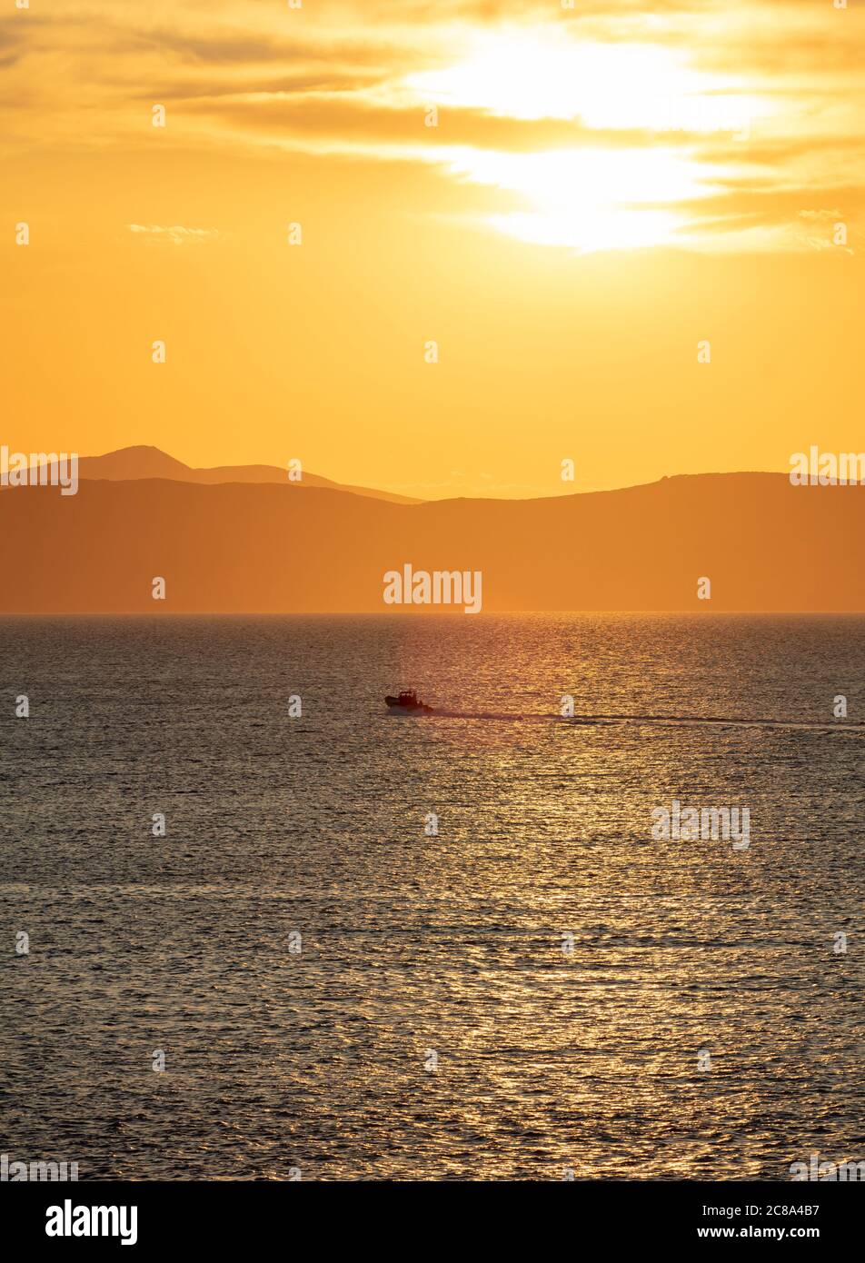 Sunset orange cloudscape over sea water. Dramatic magical sunrise seascape in Aegean sea Greece. Dark island land horizon, twilight, dawn background. Stock Photo