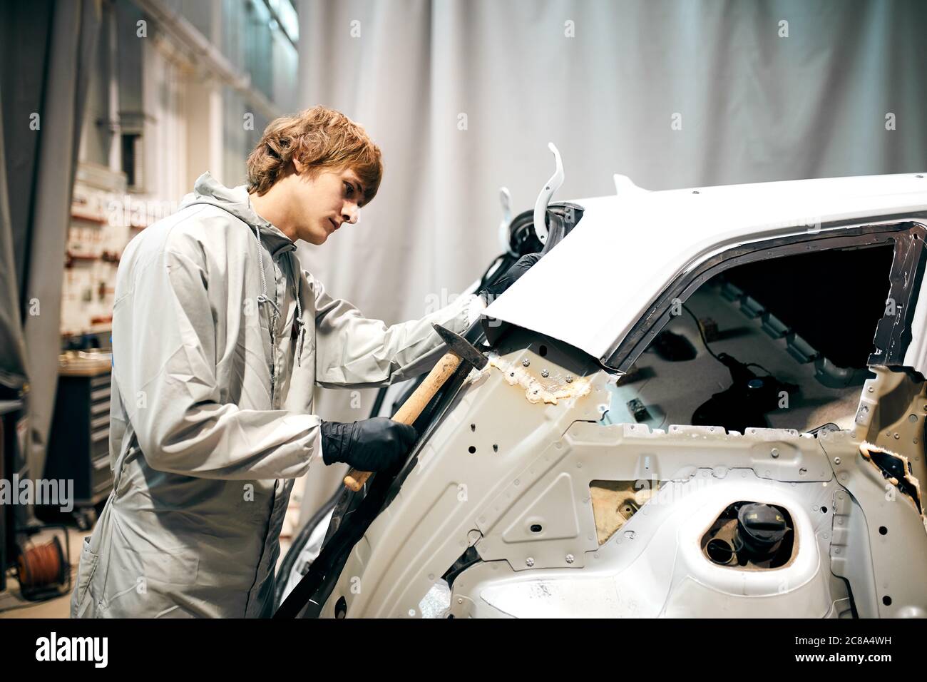 auto-garage-worker-flatten-metal-body-car-with-hammer-in-automotive