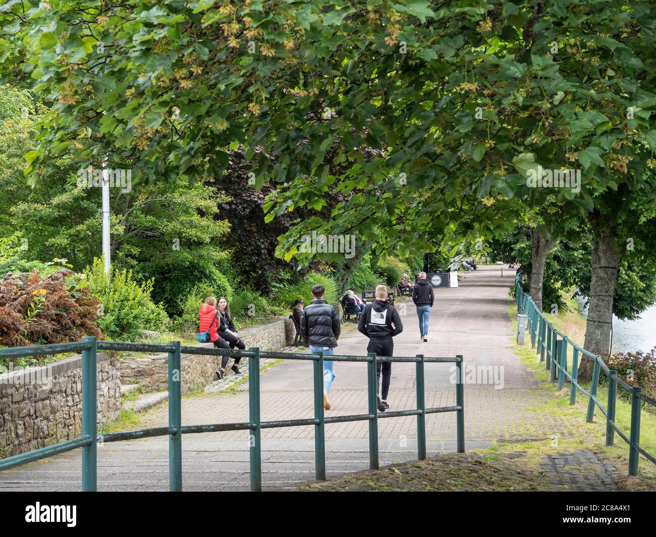 People walking and sitting on the tree lined riverside path by the River Ness. Ness Walk, Inverness, Scotland Stock Photo