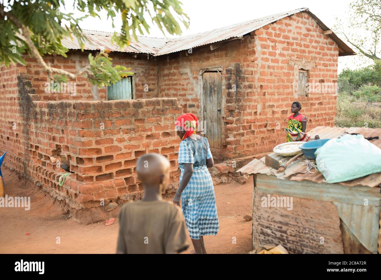Regina Mwangangi (65), her daughter-in-law Mary Muinde (20), and granddaughter Teresia Monica (11), stand outside their home in Makueni County, Kenya. Stock Photo